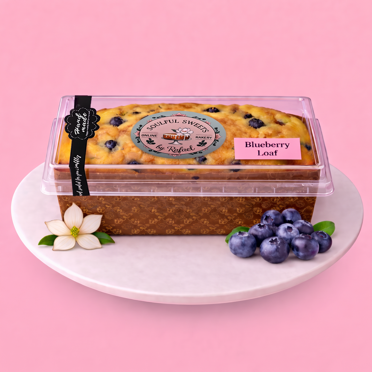 Soulful Sweets by Rafael blueberry loaf cake in a clear plastic container on a white plate with fresh blueberries.