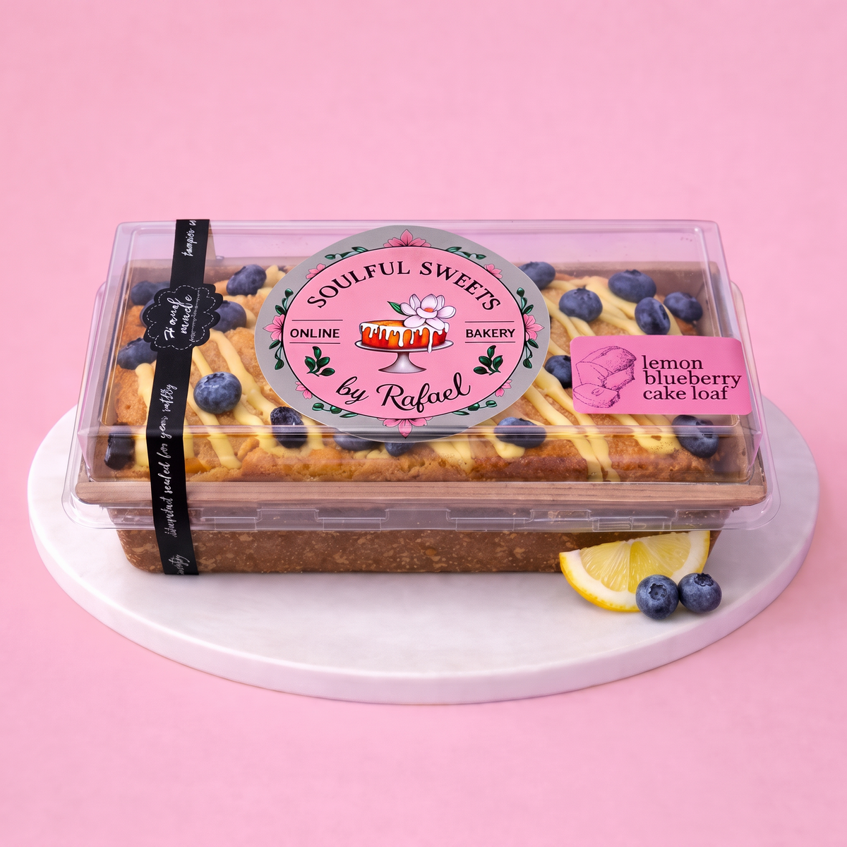 Soulful Sweets by Rafael lemon blueberry cake loaf in a clear display box with lemon glaze and fresh blueberries.