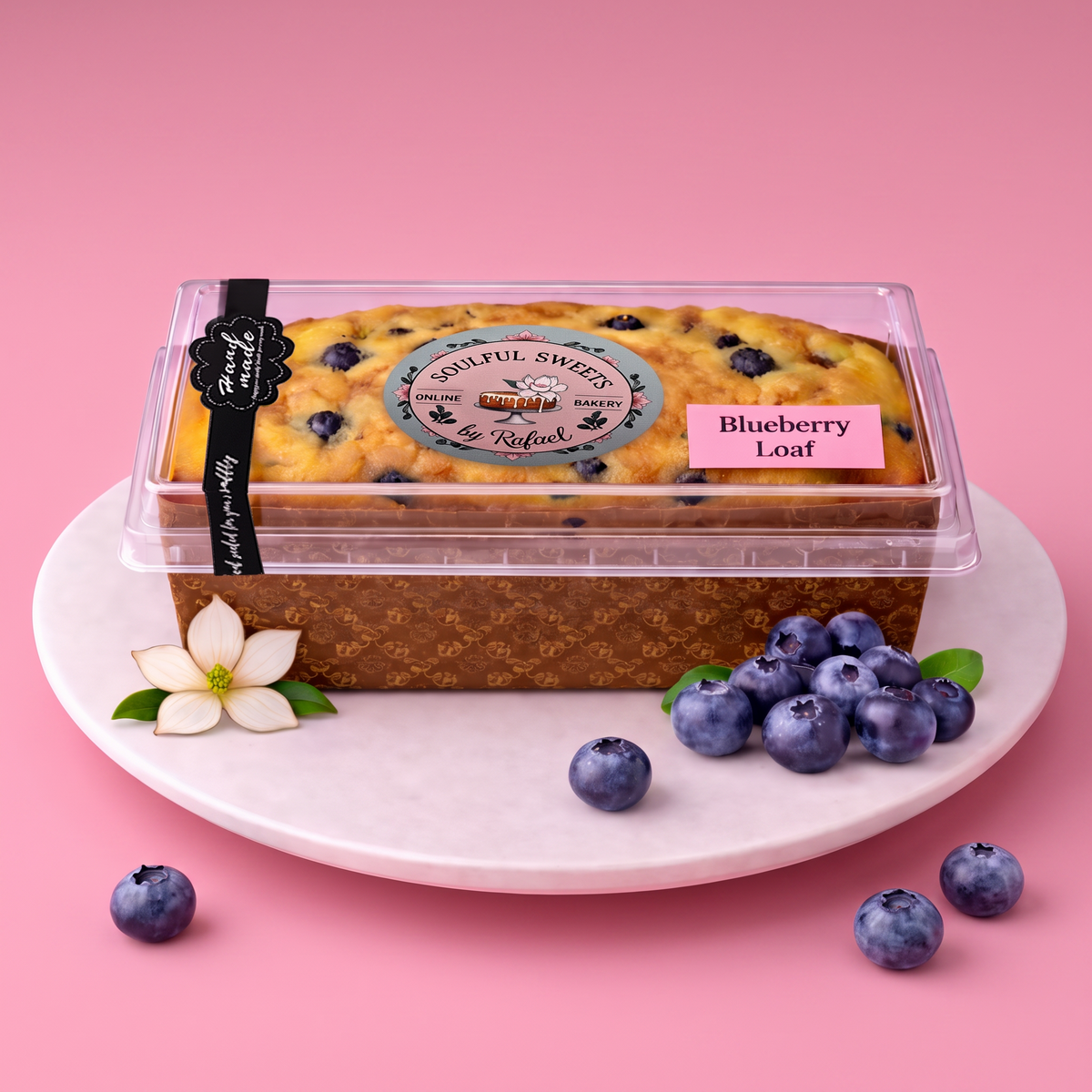 Soulful Sweets by Rafael blueberry loaf in a clear plastic container on a white plate with fresh blueberries.