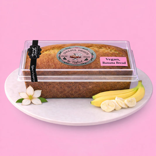Soulful Sweets by Rafael vegan banana bread loaf in a clear plastic container with fresh bananas on a white plate.